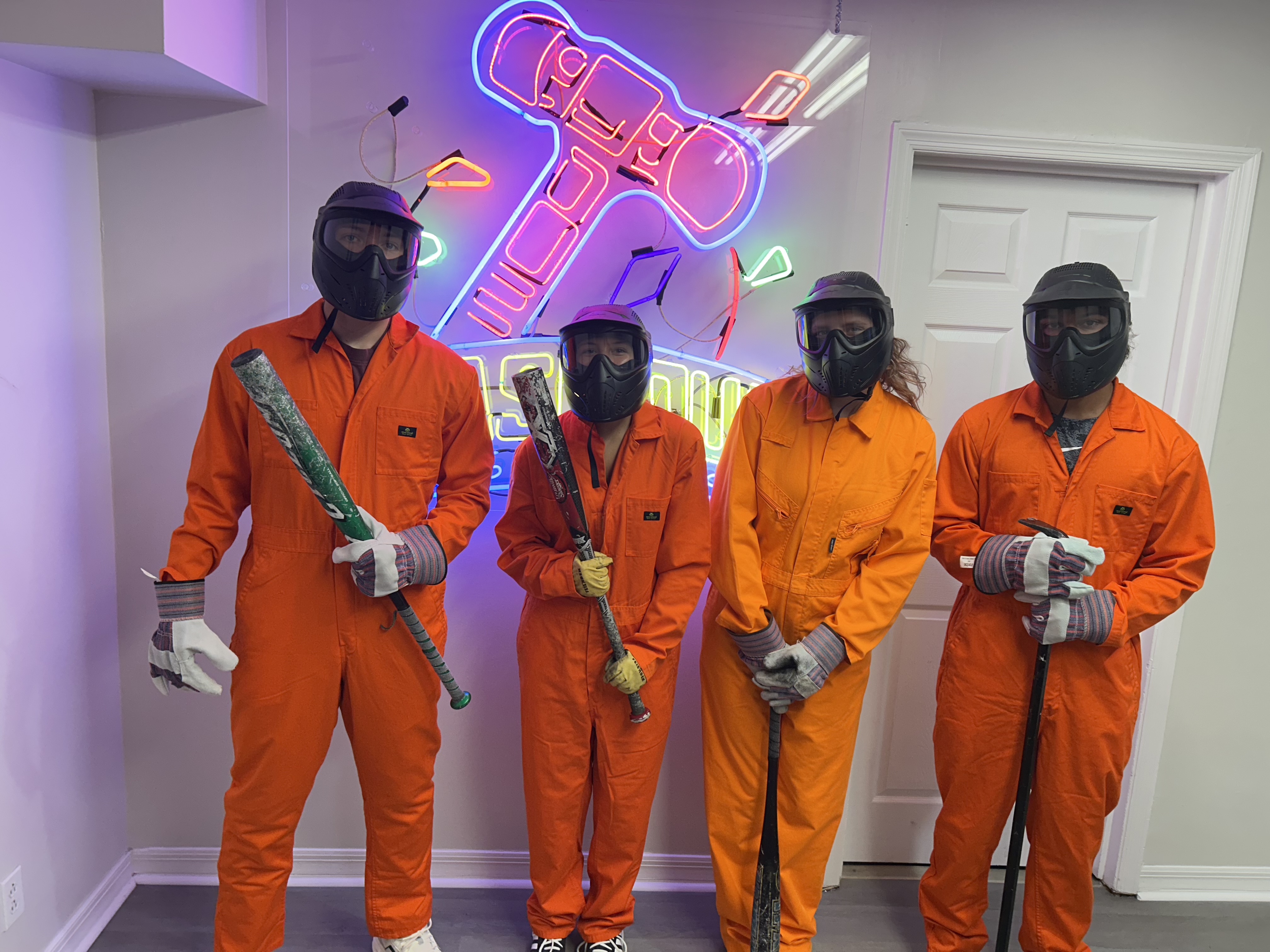Crash Out Rage Rooms customers in orange jumpsuits and protective gear selecting bats from a barrel of smash tools