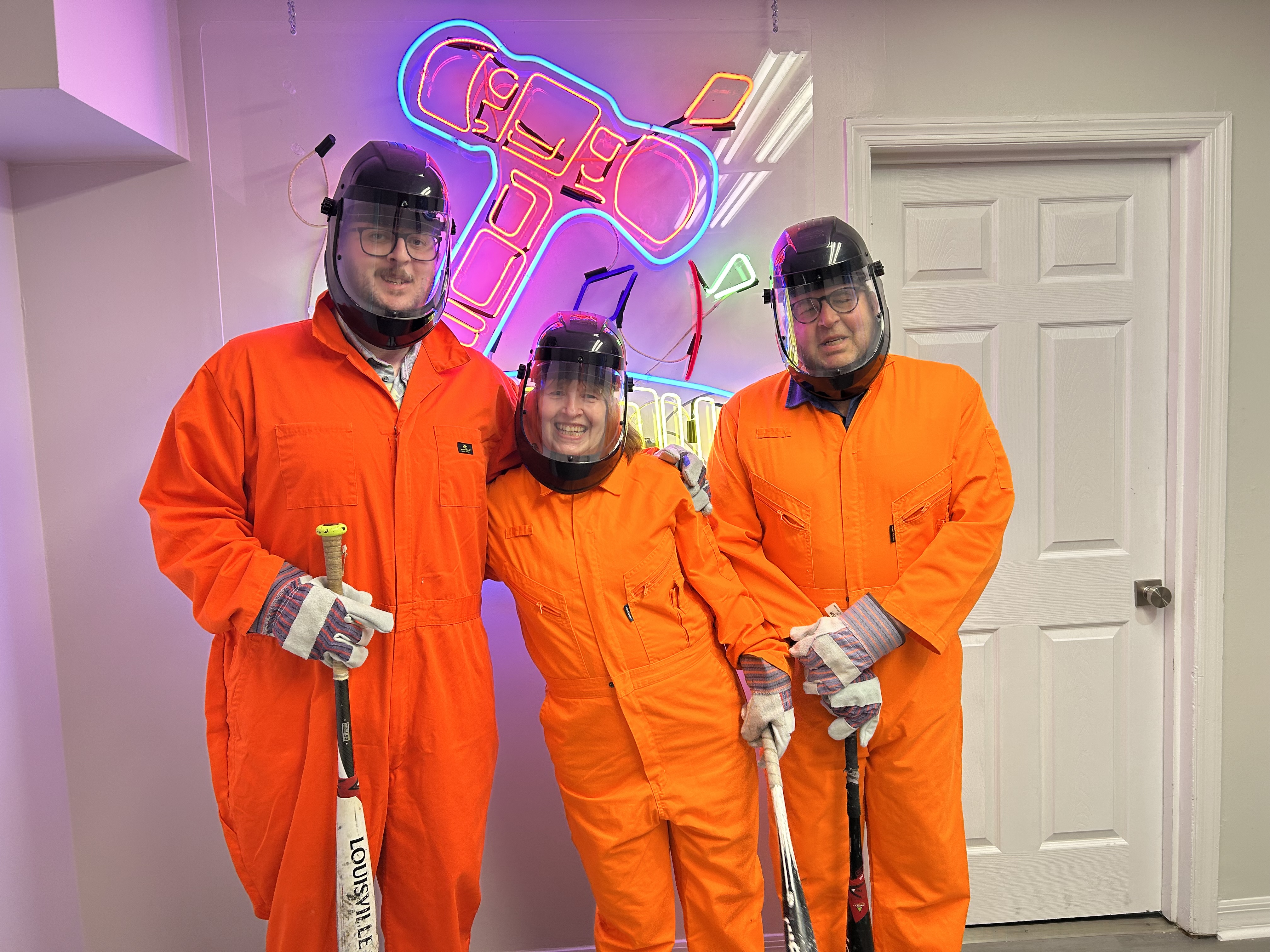 Three Crash Out guests in orange jumpsuits and face shields smiling before entering the smash room
