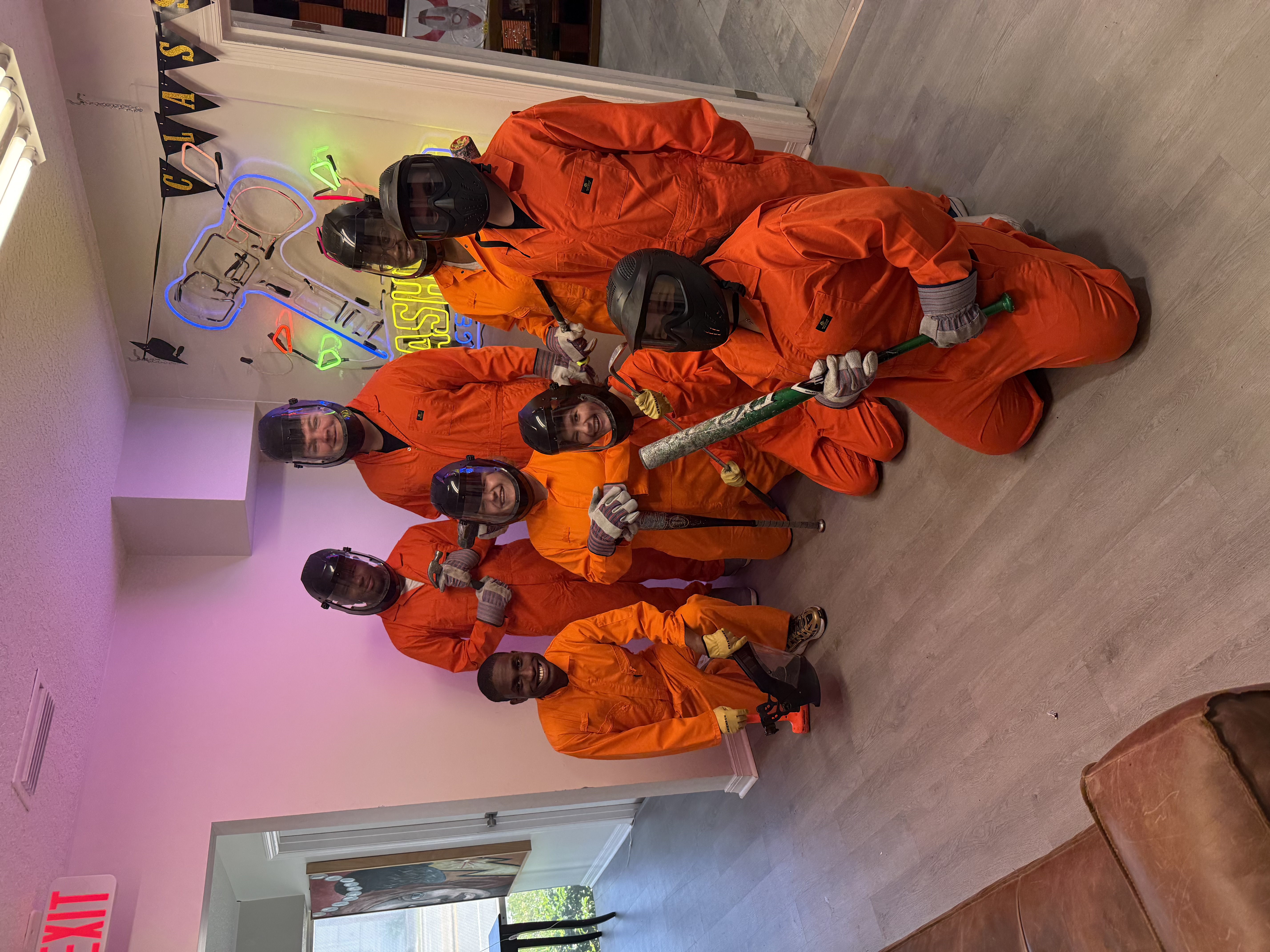 Eight Crash Out guests in full orange protective gear posing before their smash room session