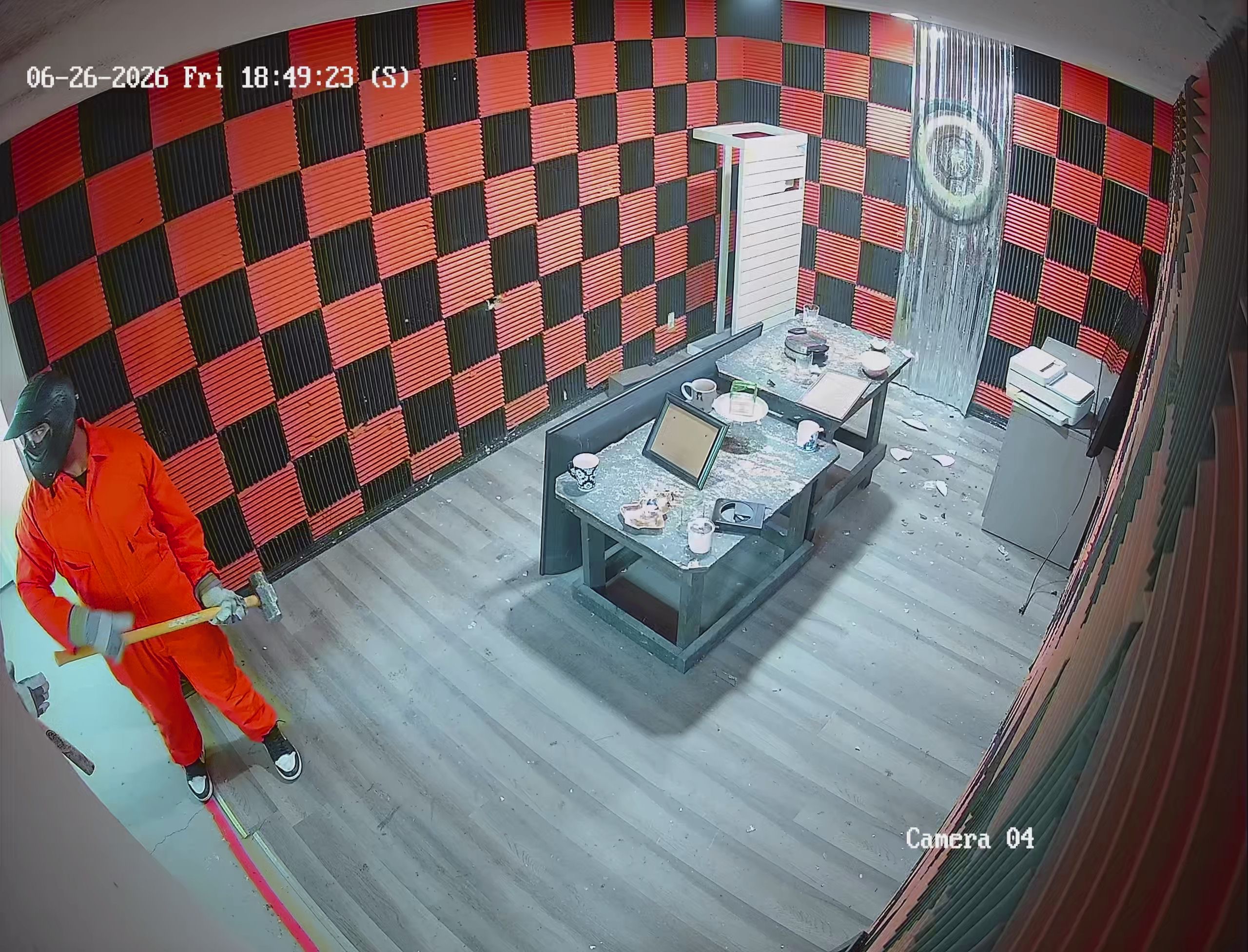 Security camera footage of Crash Out Rage Rooms customer in orange jumpsuit swinging sledgehammer inside red and black checkered smash room