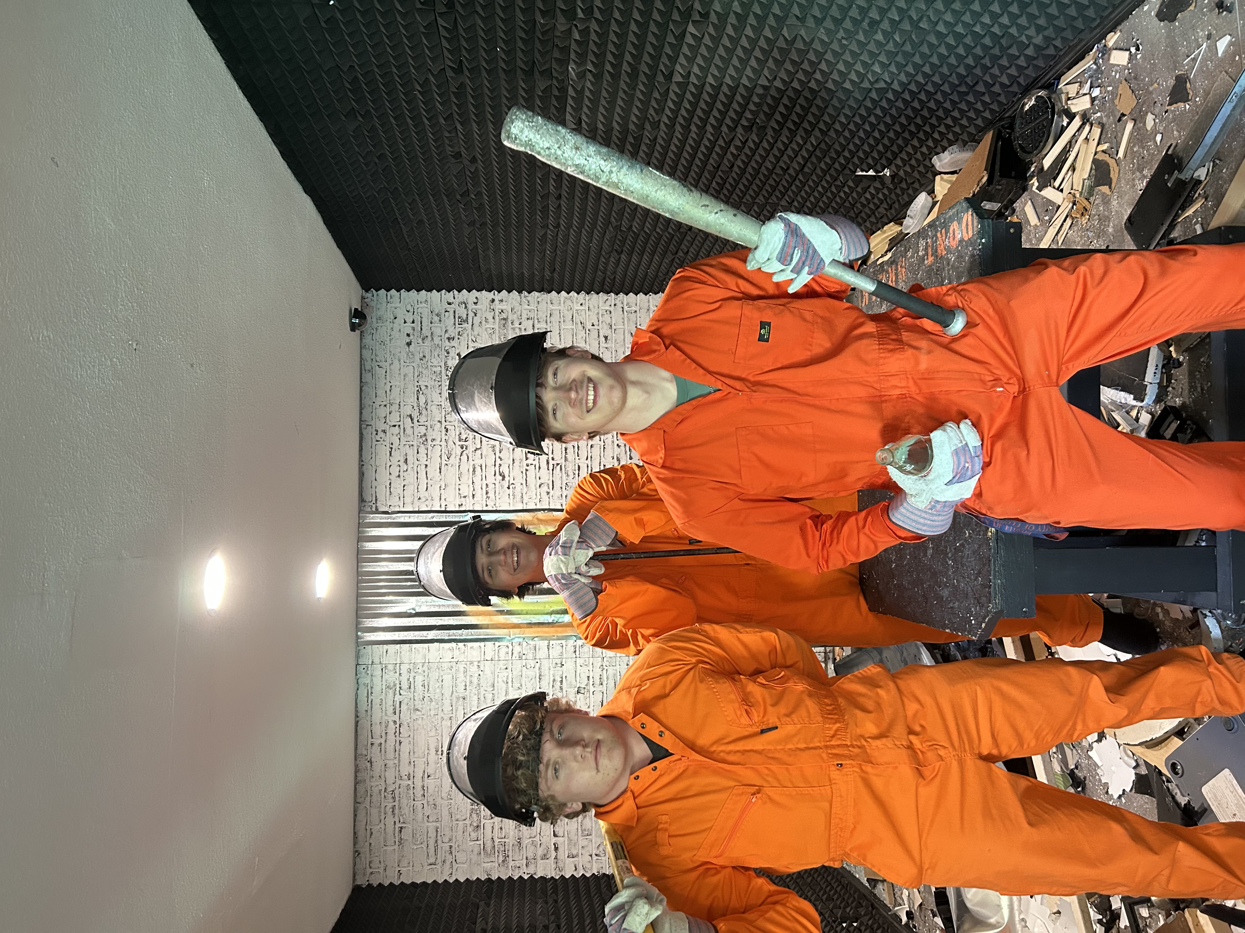 Three Crash Out customers celebrating inside smash room surrounded by broken electronics and debris
